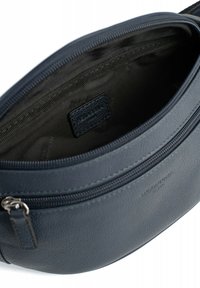 Interno di una borsa in pelle blu scuro caratterizzato da una texture liscia, chiusura con zip e un piccolo etichetta impressa sulla fodera.