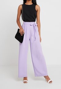 Czarna bezrękawnik połączona z wysokim stanem lawendowymi spodniami w szerokim kroju, z wiązaniem z przodu. Uzupełniona małą czarną torebką i białymi obcasami.