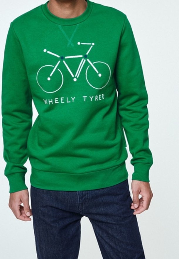 Zelená mikina s jednoduchou bílou grafikou bicyklu a textem "WHEELY TYRED", kterou nosí osoba s tmavými džíny.