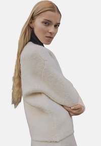 Pull en laine blanc surdimensionné avec une finition texturée et un col roulé noir. Présente une coupe décontractée et des épaules tombantes, améliorant le confort.