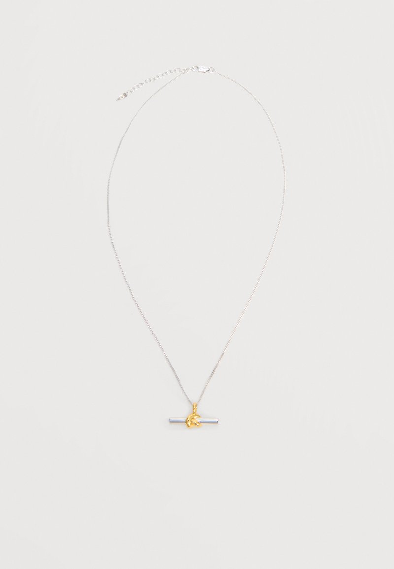 Λεπτό ασημένιο κολιέ με αλυσίδα και οριζόντιο ασημένιο μενταγιόν σε σχήμα μπάρας, τυλιγμένο με μια μικρή χρυσή λεπτομέρεια σε κόμπο.