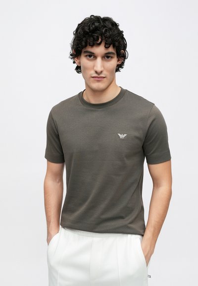 Olivovo zelené tričko s krátkym rukávom a okrúhlym výstrihom, s textúrovaným logom na ľavej hornej strane hrude. Hladká látka, priliehavý strih.