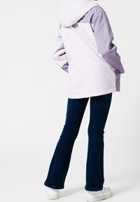 Světle fialová bunda s kapucí a tmavšími fialovými akcenty na ramenou, v kombinaci s tmavými rozšířenými džíny a bílými teniskami, na bílém pozadí.