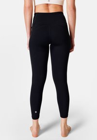 Leggings neri a vita alta con una superficie liscia, cuciture curve e dettaglio riflettente del logo sulla caviglia. Progettati per comfort e flessibilità.