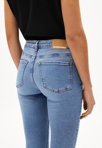 Jeans skinnies azules deslavados hechos de denim, con cintura alta, cuatro bolsillos y una etiqueta de cuero marrón en la parte trasera con "ARMEDANGELS."
