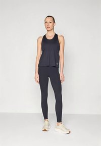 Fekete ujjatlan felső, laza szabású, szűk fekete leggings-szel párosítva. Lábbeli világos színű tornacipő. Egyszerű dizájn, látható minták nélkül.