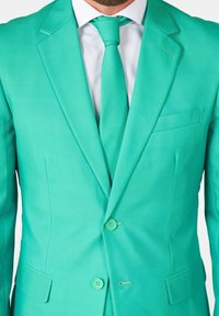 Giacca da abito turchese con due bottoni, revers a punta e una tasca sul petto. Abbinata a una cravatta coordinata e una camicia bianca.
