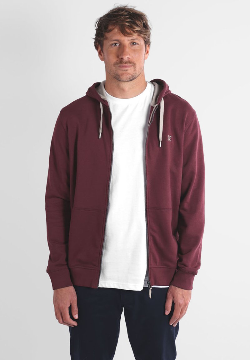 Sweat à zip bordeaux avec un cordon gris, deux poches avant et un t-shirt blanc à col rond en dessous ; tissu doux, design décontracté.
