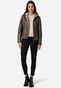 Brun läderjacka med pälsfoder och huva, kombinerad med en krämfärgad tröja och svarta skinny jeans, bärs med svarta ankelskor.