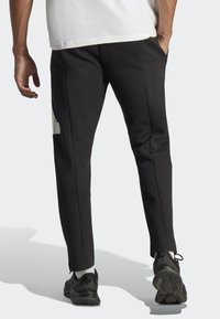 Svarta joggerbyxor i mjukt tyg med sidofickor, smalnande ben och en subtil logotyp på höften. Matchas med svarta skor.