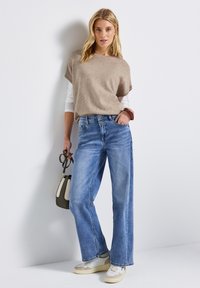 Beige gebreide top met korte mouwen, gecombineerd met lichtblauwe wijde jeans. Geaccentueerd met een kleine handtas en witte sneakers.