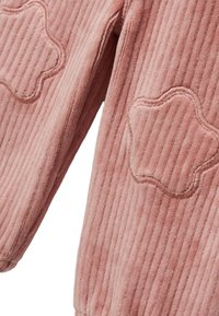 Veste en velours côtelé rose avec une texture côtelée et un détail brodé en forme d'étoile sur la manche. Tissu doux avec une apparence chaleureuse.