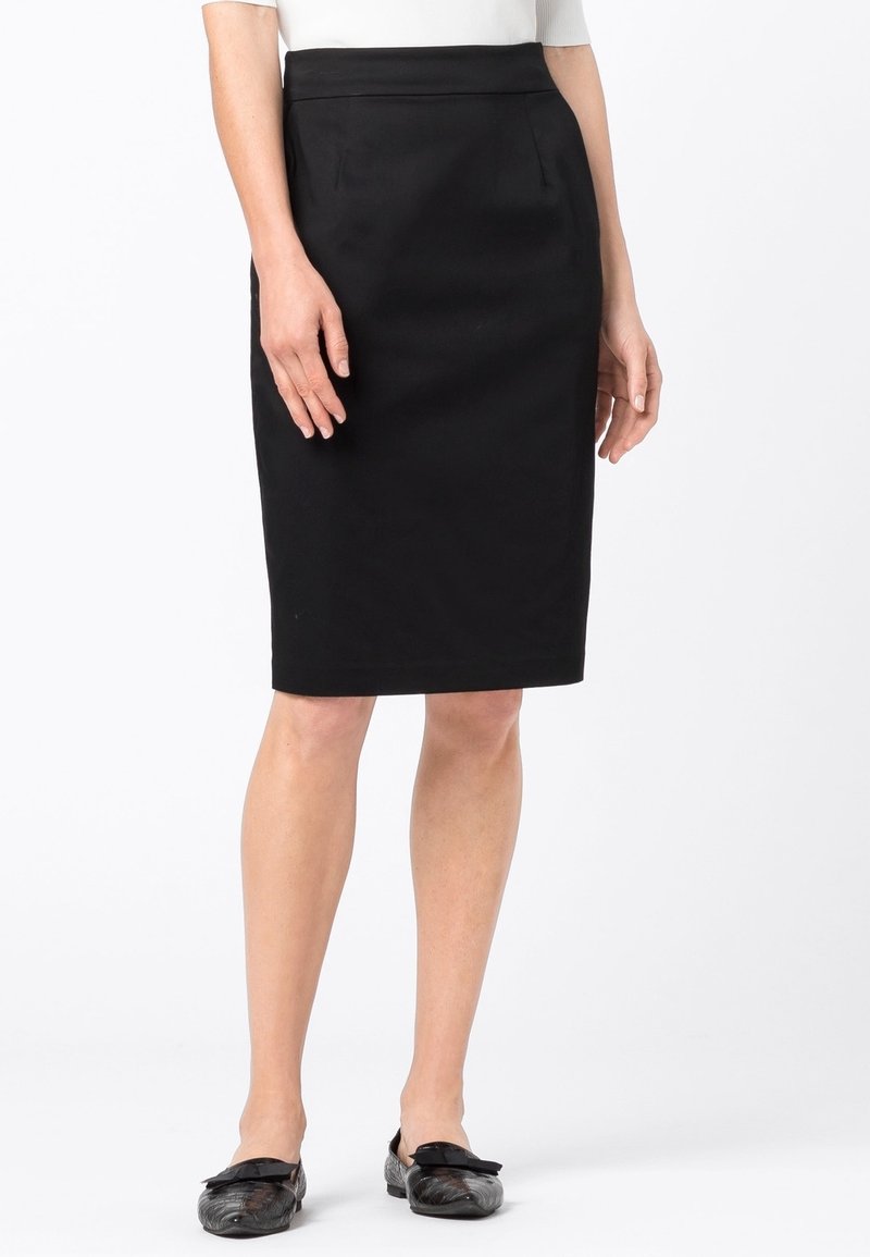 Černá tužková sukně se hladkou texturou, zúženým tvarem a předními kapsami. Nosená s černými botami se zdobením ve tvaru mašle.