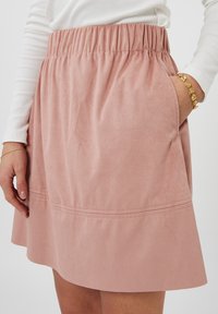 Gonna rosa blush realizzata in morbido tessuto simil suede, con vita elastica e tasche laterali, orlo svasato e dettagli cuciti.