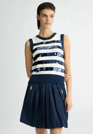 Top senza maniche blu e bianco in maglia con strisce orizzontali di paillettes. Abbinato a una gonna plissè blu scuro con zip laterali.