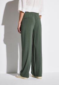 Szerokie, oliwkowe spodnie z gładkiego, lekkiego materiału. Posiadają elastyczny pasek w talii oraz dwie tylne kieszenie. Doskonale komponują się z casualowym obuwiem.
