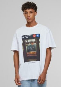 Hvid t-shirt med et grafisk motiv af en subway-dør med teksten "Memory Lane" og "UP", der fremhæver klare farver og en struktureret baggrund.