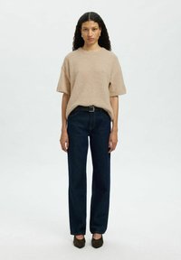 Pull en tricot beige surdimensionné avec des manches courtes, associé à un jean droit bleu foncé et des chaussures à talons marron foncé.
