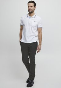 Balta polo krekla ar melniem un ziliem akcentiem, ar krūšu kabatu un trim dekoratīviem pogām. Saskaņota ar pielāgotām tumšām biksēm un melnām kurpēm.