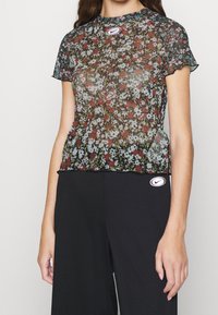 Průhledné květinové tričko s kulatým výstřihem a krátkými rukávy, s mnohobarevným květinovým vzorem na černém pozadí a nášivkou s logem Nike.