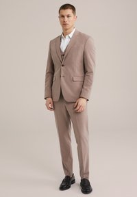 Világosbarna szabott öltöny, egysoros zakóval, slim-fit nadrággal és alatta fehér inggel. Fekete loaferek zárják le az öltözetet.