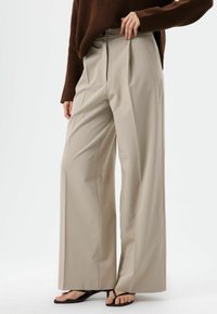 Beige wijde broek met voorplooien, een gladde textuur en een getailleerde pasvorm, gestyled met een bruine trui en zwarte sandalen.