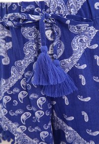 Niebieskie szorty w wzór paisley, z teksturowanej tkaniny, z wiązaniem na sznurku ozdobionym dwoma niebieskimi frędzlami.