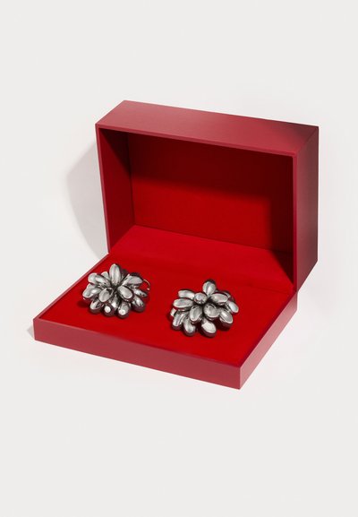 Ασημένια σκουλαρίκια σε σχήμα λουλουδιού με ομαλές, πεταλοειδείς λεπτομέρειες, παρουσιάζονται σε κόκκινο κουτί με μαλακή εσωτερική επένδυση.