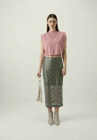 Rozā īsā krekla bez piedurknēm apģērbs apvienots ar garu, sudrabaini mirdzošu svārku. Beiģu potīšu zābaki un mazs beiģu rokassomas papildina tēlu.