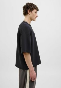 Sort oversized t-shirt med korte ærmer, glat tekstur, rund halsudskæring og detalje langs siden, paired med grå bukser med en sidestribe.