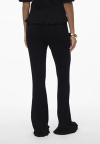 Pantalons noirs côtelés avec des jambes évasées, dotés d'un ourlet froncé. Le matériau semble texturé et ajusté, adapté pour une tenue décontractée.