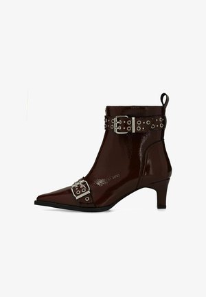 Bottines en cuir verni bordeaux avec un bout pointu, accents en métal argenté, sangles à boucles ajustables, et un talon de hauteur moyenne.