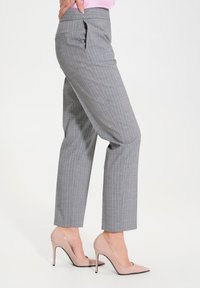 Pantaloni grigi a righe sottili con vestibilità su misura, dotati di una tasca laterale e di una texture liscia. Indossati con scarpe con tacco alto di colore chiaro.