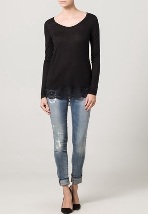 Top negro de manga larga con escote redondeado y encaje en el dobladillo, combinado con unos jeans ajustados rasgados de color azul claro y tacones negros.