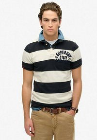 Gestreepte polo in marineblauw en wit, met een denim kraag. Draagt met kaki broek en een bruine riem. Casual ontwerp met logo-details.