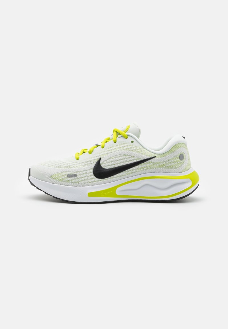 Bílé sportovní boty s vrškem z síťoviny, černým logem swoosh, neonově zelenými akcenty, texturovaným designem a polstrovanou podrážkou.