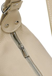 Beige leren handtas met een textuur oppervlak, zilveren rits en contrasterende witte stiksels. Voorzien van metalen hardware en een ronde vorm.