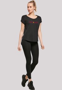 Svart t-skjorte med "GRYFFINDOR" i rød skrift, kombinert med svarte leggings og svarte joggesko, som har en avslappet passform og korte ermer.