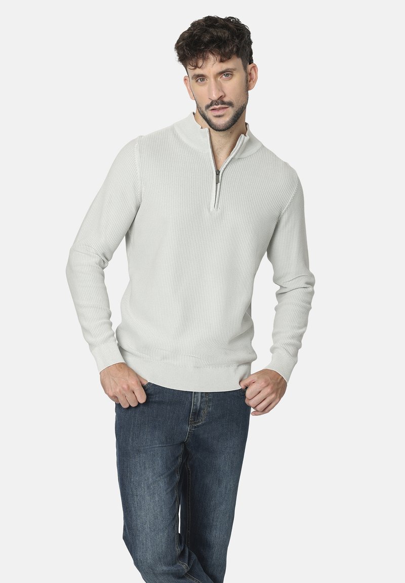 Suéter de punto gris claro con collar de media cremallera, textura acanalada y puños ajustados, combinado con jeans de mezclilla azul oscuro.