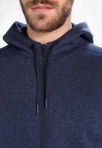 Felpa con zip di colore blu navy realizzata in tessuto testurizzato, dotata di cappuccio con cordino e due dettagli con zip sul davanti.