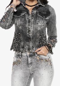 Musta farkkutakki, jossa on kulutetut hihat ja korukivikoristeet. Yhdistetty harmaisiin farkkuihin, joissa on strassikoristeet taskuissa.