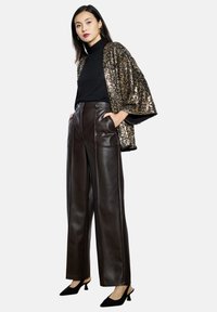 Rjave visokotlačne hlače iz umetnega usnja z vertikalnimi šivi, v kombinaciji s črno turtlenecko in zlate bleščice kimono-style jakno. Črne pete.