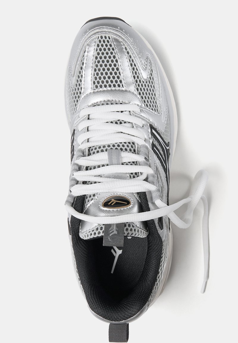 Baskets de sport argentées avec des superpositions en mesh et en synthétique, lacets blancs, intérieur noir et un accent logo sur la languette.