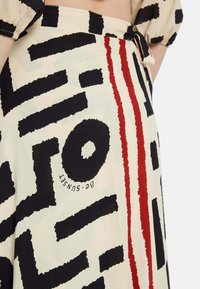 Falda de tela estampada en crema, con gráficos negros llamativos y rayas rojas. Material ligero, con un detalle de lazo en la cintura.