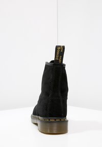 Botas de tobillo de ante negro con puntera redonda, suela de goma y costuras de acento amarillas. Cuenta con una lengüeta con el texto "CON SUELAS CON RESORTE".