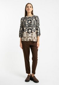 Bluzka z długim rękawem z wzorem damaskowym w kolorze kremowym i granatowym, zestawiona z brązowymi spodniami typu tapered i brązowymi zamszowymi butami wsuwanymi.