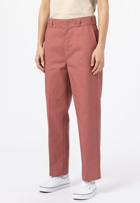 Růžové kalhoty s rovnými nohavicemi, vysokým pasem, bočními kapsami a poutky na opasek, doplněné o bílé tenisky. Hladká textura látky.