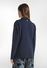 Laivastonsininen pitkähiha paita, jossa on kauluksellinen muotoilu ja pehmeä kangas. Takana näkyy saumadetalji, ja se on yhdistetty kuviollisiin housuihin.