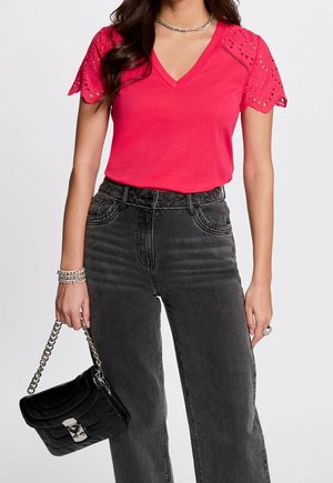 Różowy t-shirt z dekoltem w kształcie litery V i krótkimi rękawami z ażurowej koronki, zestawiony z wysokim stanem czarnych dżinsów oraz usztywnioną czarną torebką na łańcuszkowym pasku.