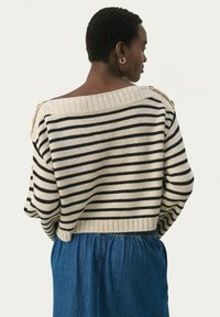 Pull rayé en crème et noir, avec un col large en côtes et des manches courtes. Matière tricot douce, associé à une jupe en denim.